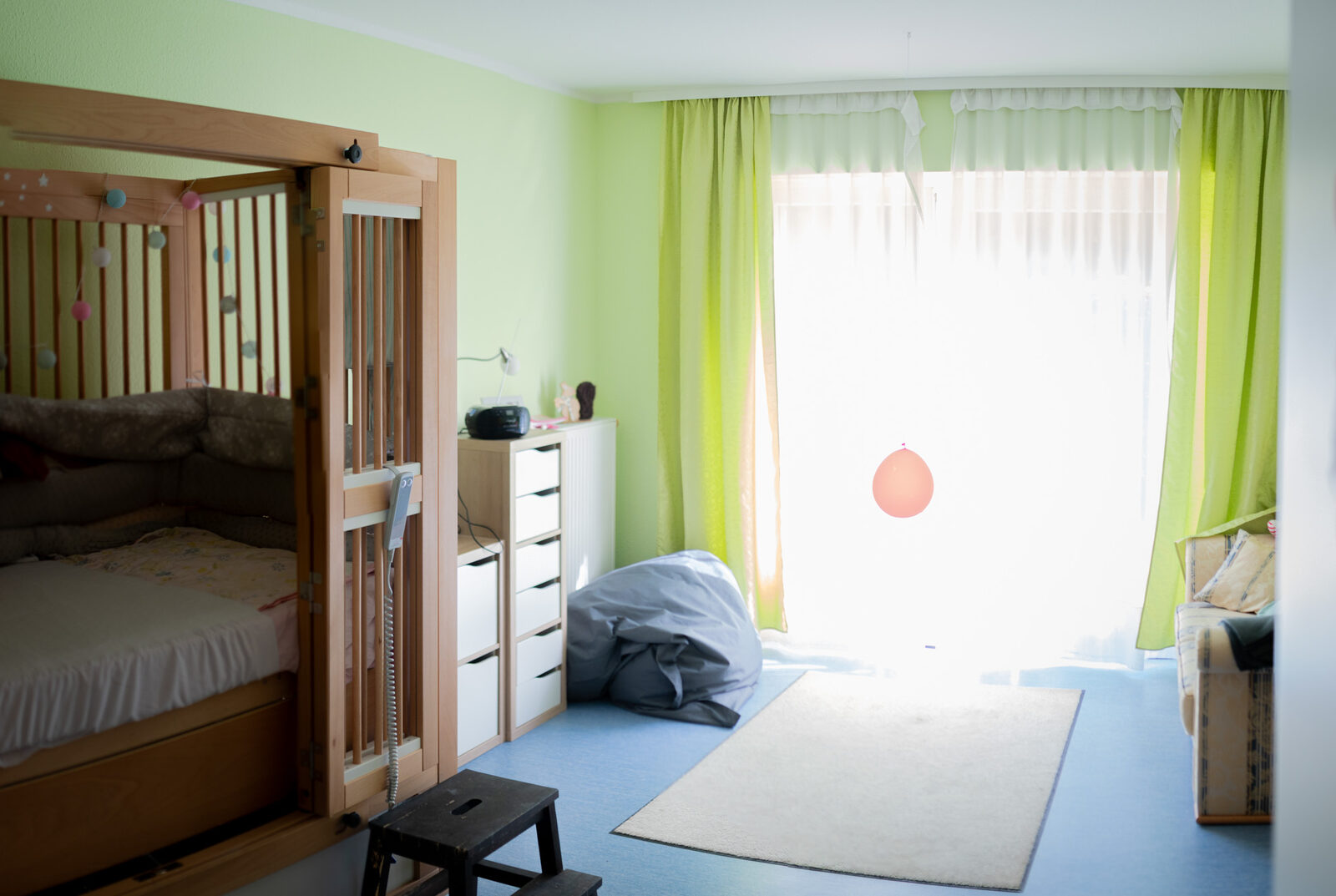 Helles Einzelzimmer mit Pflegebett, Regalen und großem Fenster.